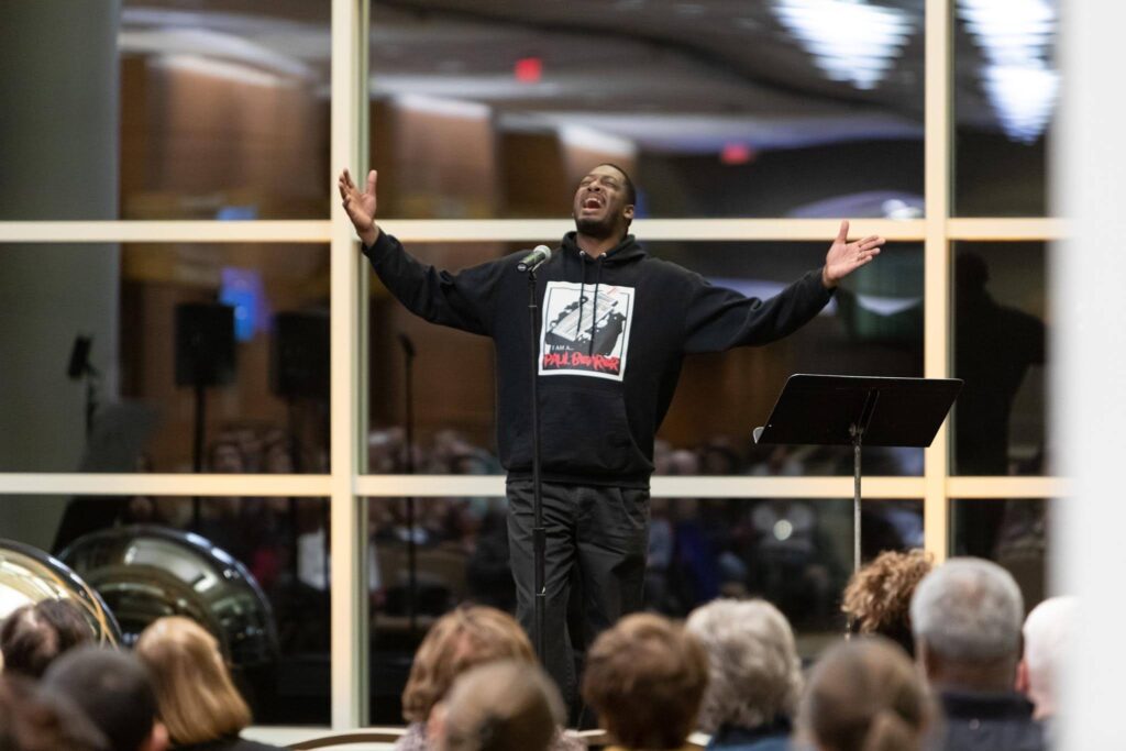 Frank Sentwali with his arms out performing for a crowd.