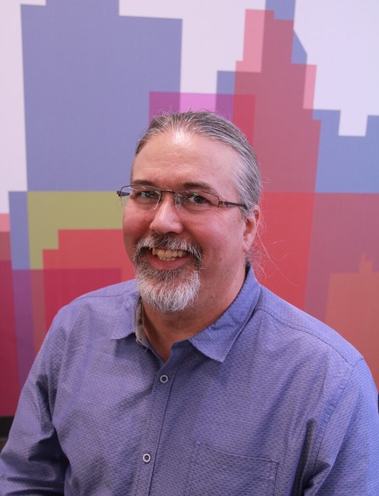 headshot of man looking at camera, smiling wearing a button up shirt