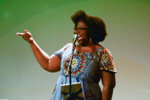Kashimana at a microphone singing with a smile.