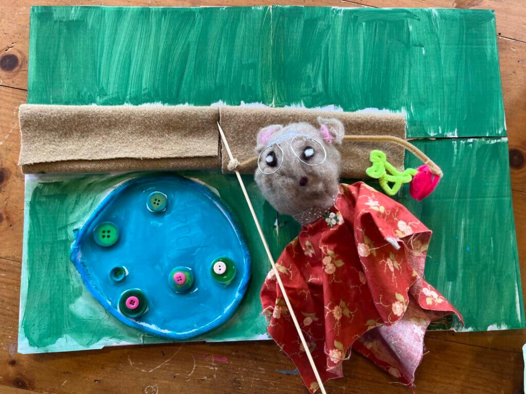 A mouse puppet with a background of recycled materials.