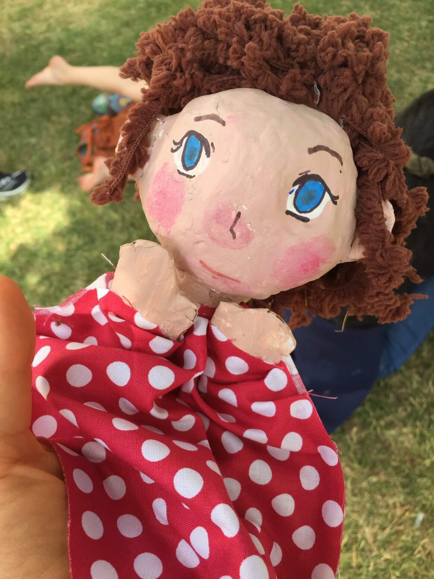 Paper mache puppet of a girl with brown hair and a red polka dot dress. 