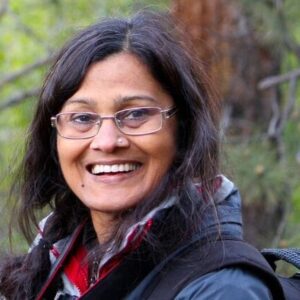 A woman wearing glasses with long dark hair smiles at the camera.