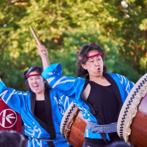 Two women in traditional dress play Taiko drums.