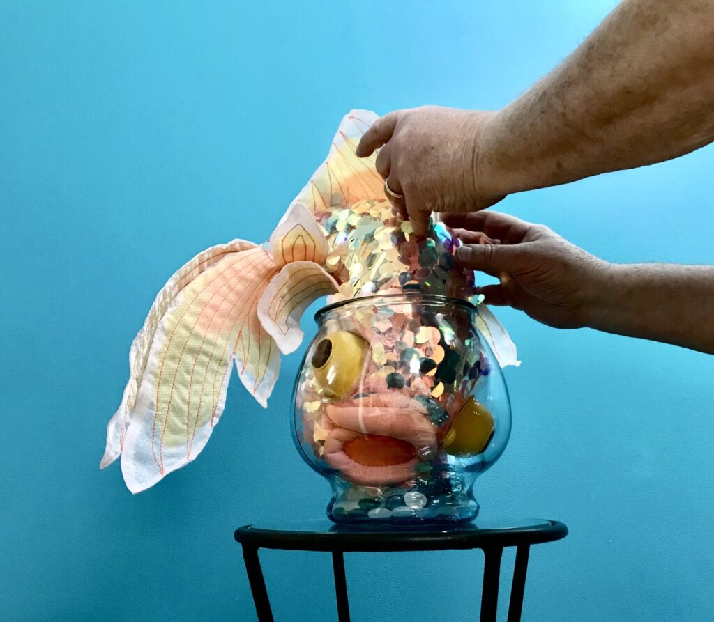 A table supporting a vase filled with tactile fabric and hands manipulating the items.