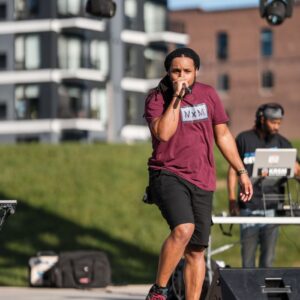 Young man in burgundy shirt performs at an outdoor concert.