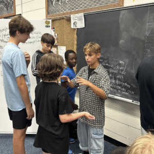 Several adolescent boys gathered in front on a chalkboard collaborating on on creative exercise.