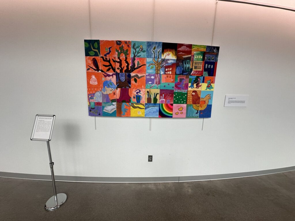 A hanging large work that is made of tiny grid art made by different people. 