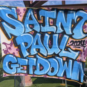 A colorful graffiti-style banner reading “Saint Paul Get Down 2024” in bold blue letters outlined with black and orange, against a background of pink and purple splashes. The banner hangs outdoors at a park event.