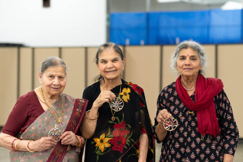 Three women smiling at the camera holding jewelry artwork they made.
