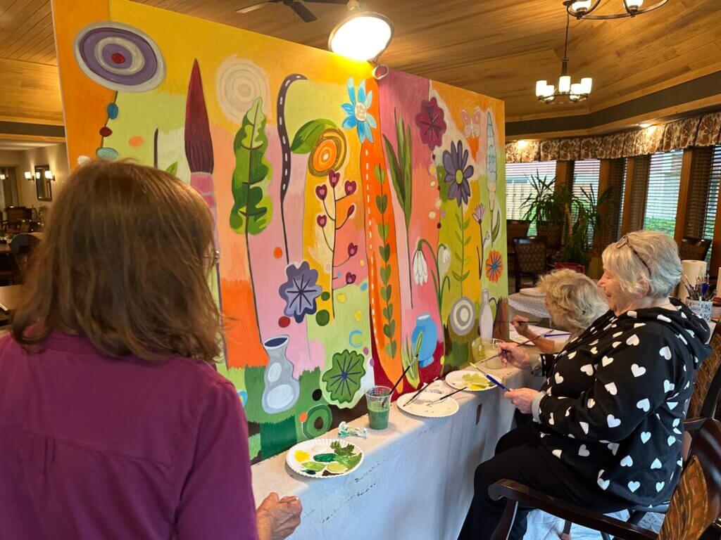 Three people work on a mural that is set up on a table. 