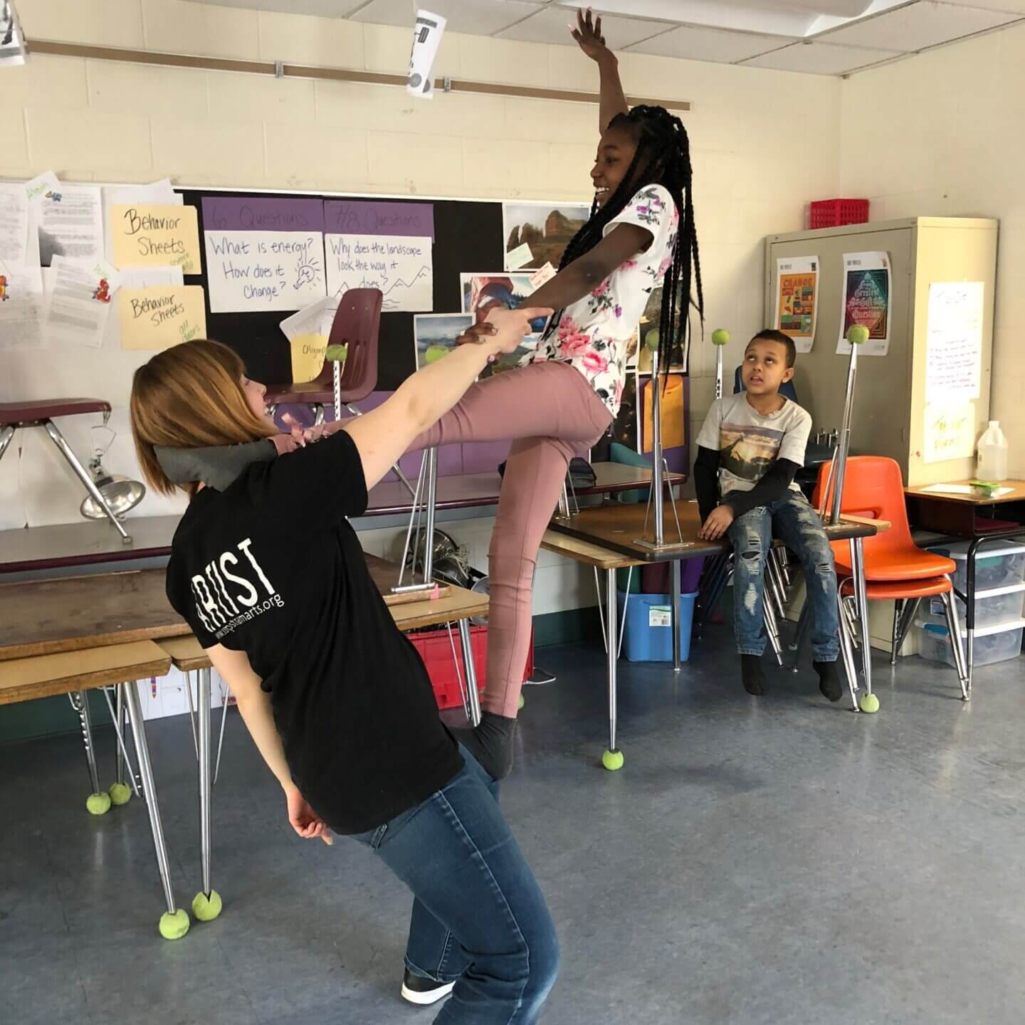 A student in a classroom on top of an adult and smiling.
