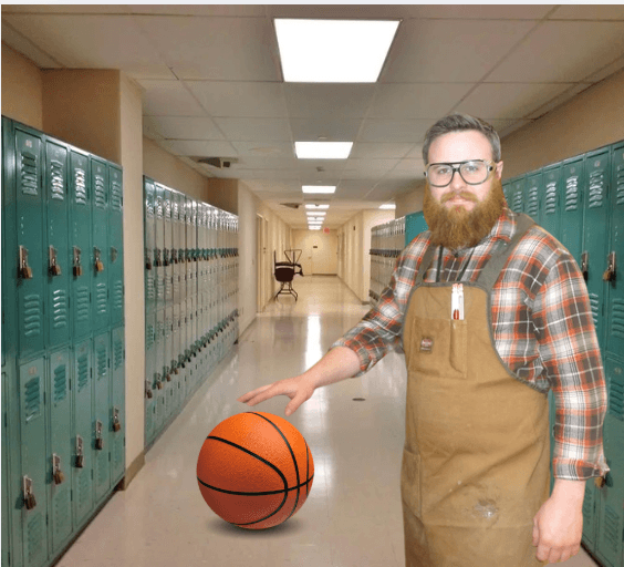 A bearded man wearing glasses, a plaid shirt, and a canvas work apron stands in a school hallway lined with lockers, resting his hand on a basketball.