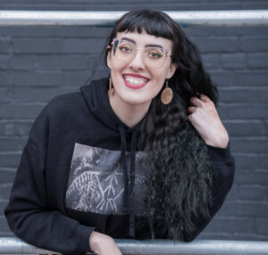 Moira, the artist, smiling at the camera in a black hoodie.