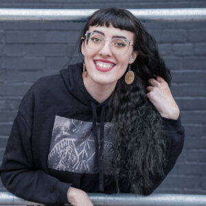 Moira, the artist, smiling at the camera in a black hoodie.