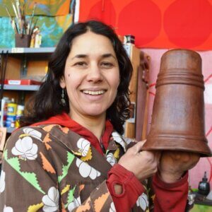 Gita holding a bell in front of a colorful art space.